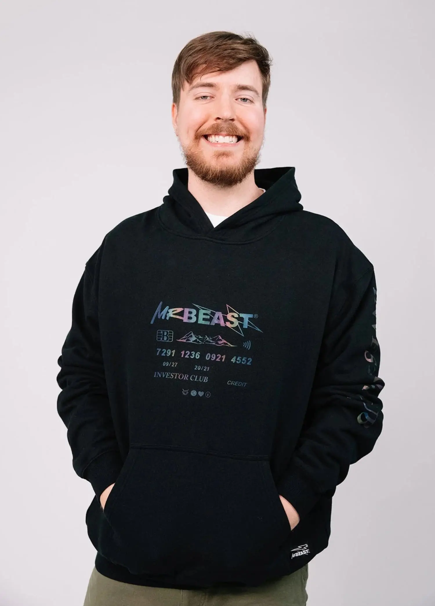 Fotografia de um homem sorridente vestindo um moletom preto da marca MrBeast, destacando o logo e detalhes do design no peito e nas mangas. Estilo casual e moderno.