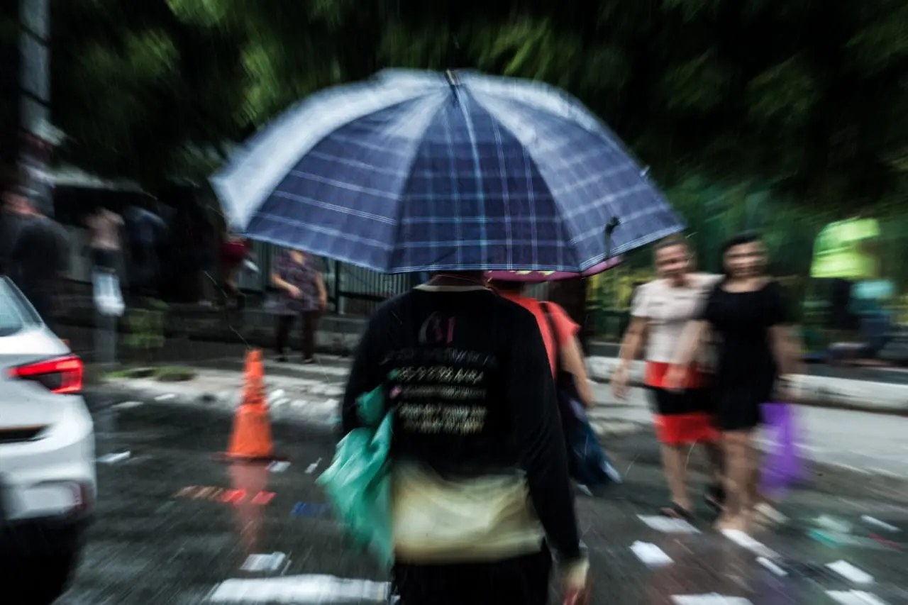 Pessoa de costas, na chuva, segurando guarda-chuvas e atravessando a rua em Fortaleza