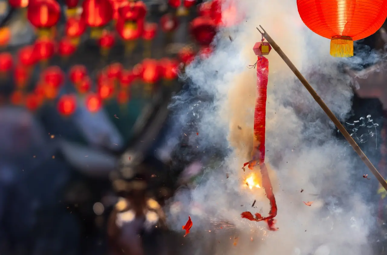 Cena vibrante do festival com lanternas chinesas vermelhas e fumaça, representando a celebração do Ano Novo Chinês.