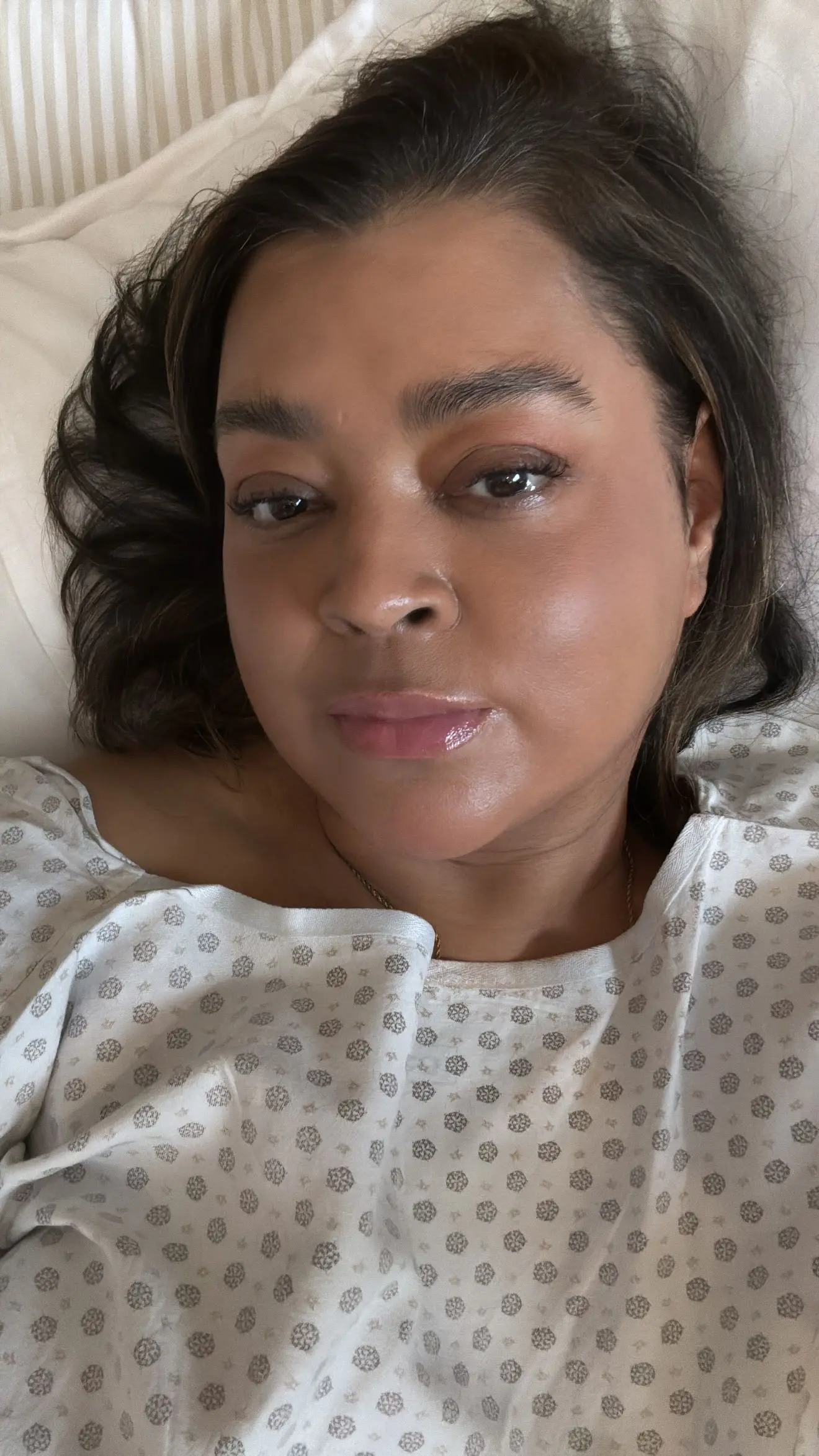 Preta Gil sorridente de cabelos soltos, vestindo um pijama hospitalar, olhando diretamente para a câmera com uma expressão serena.