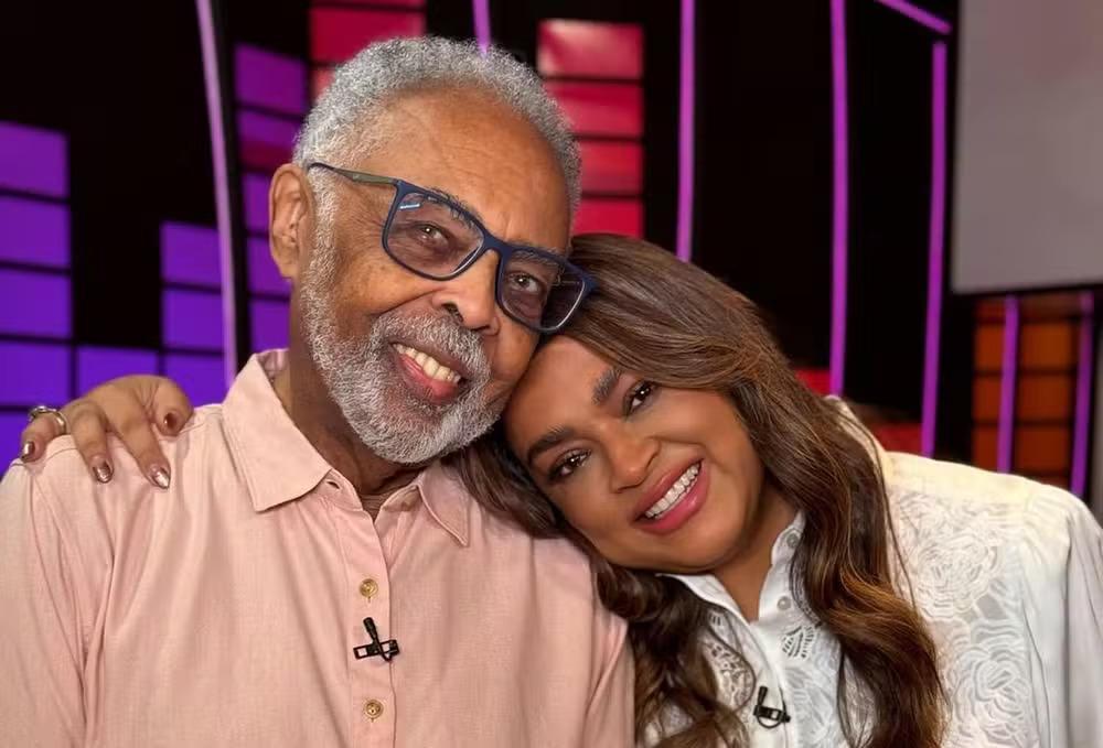 Gilberto Gil e Preta Gil sorrindo em estúdio colorido, simbolizando a música brasileira e o carinho entre pai e filha
