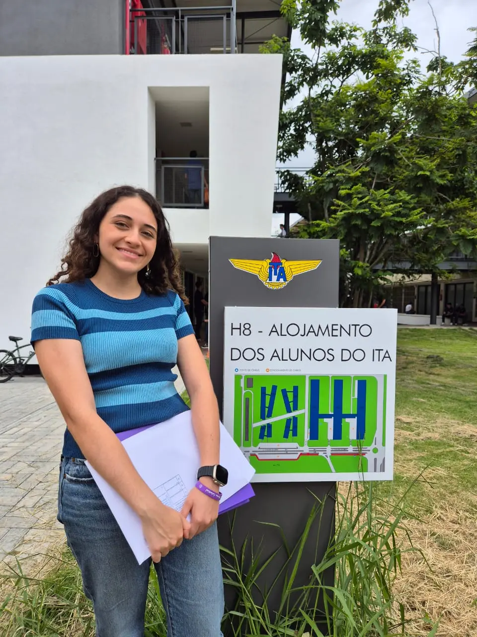 Giovanna ao lado de placa de alojamento do ITA
