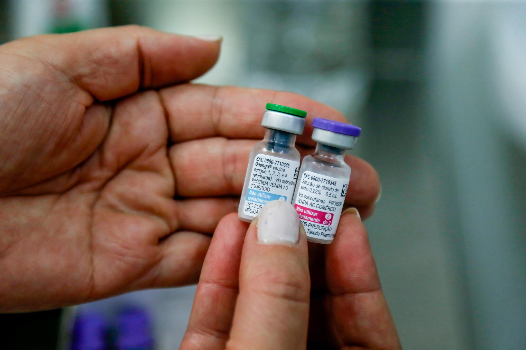 Mãos de uma mulher segurando dois frascos da vacina Qdenga, contra a dengue