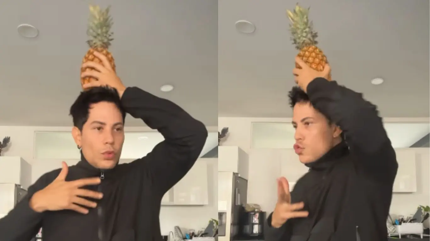 Christian Chávez posando com abacaxi na cabeça, expressando criatividade e humor em ambiente fechado.