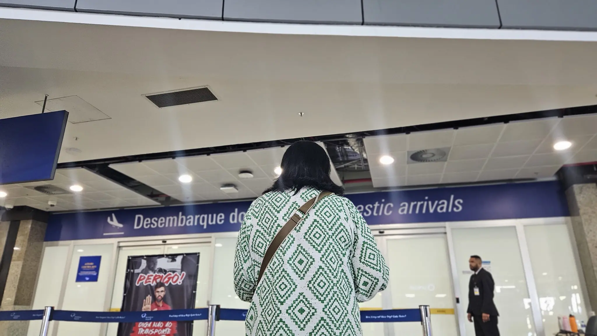 Mulher de costas espera filho que foi deportado dos EUA em frente ao portão de desembarque do Aeroporto de Fortaleza
