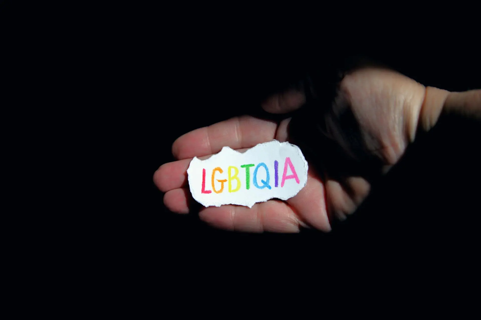 Mão segurando adesivo com o nome LGBTQIA