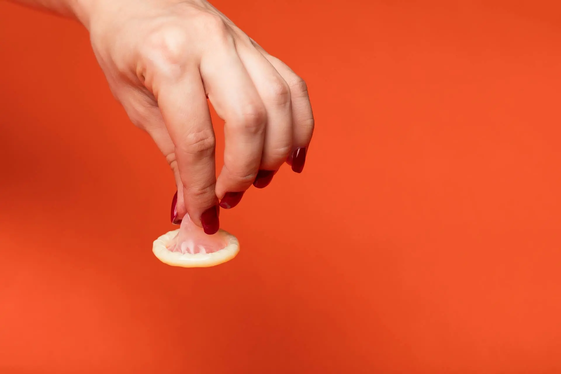 Mão segura uma camisinha pela ponta