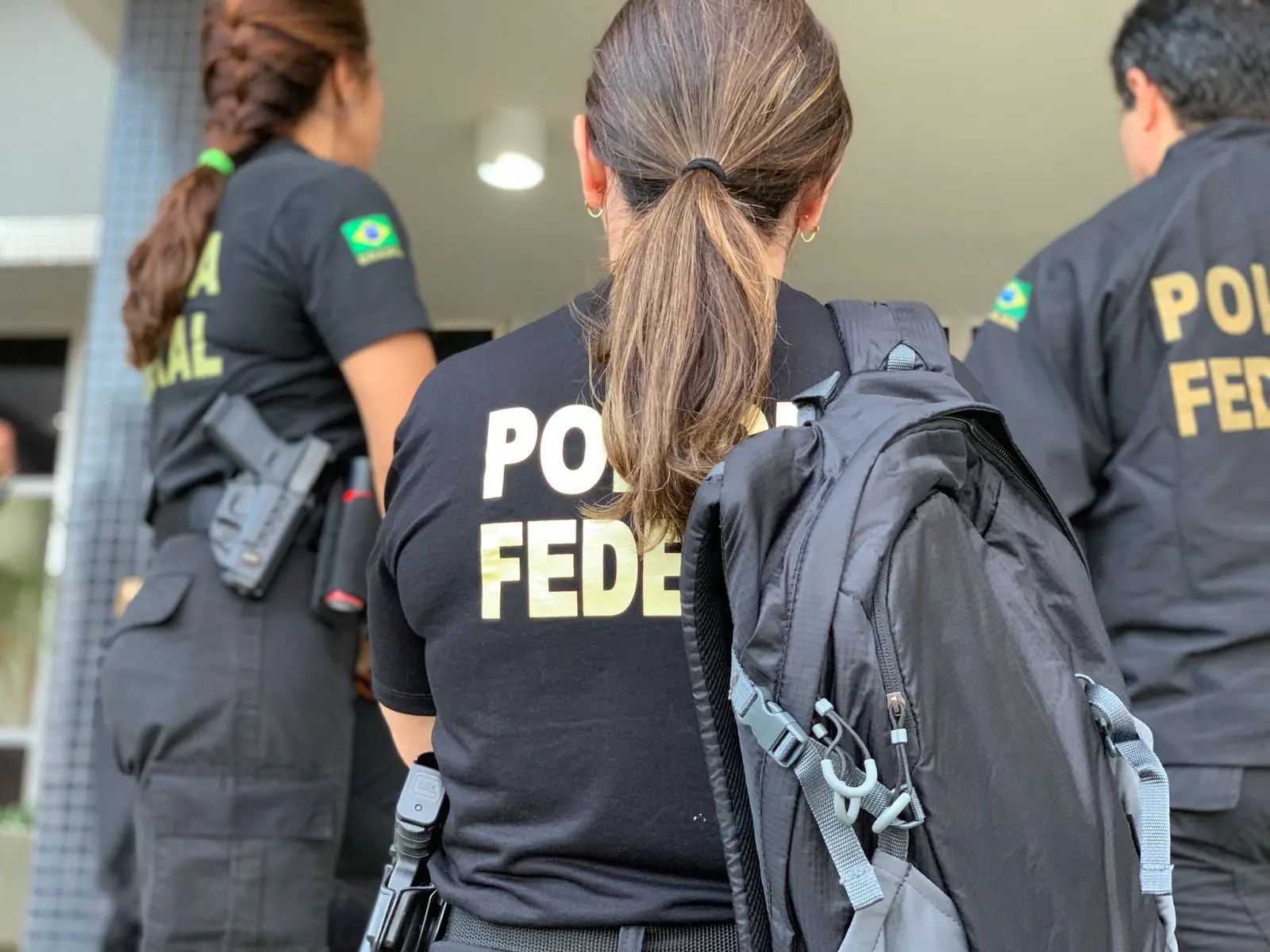 Membros da Polícia Federal do Brasil de costas, utilizando uniformes e equipamentos táticos.