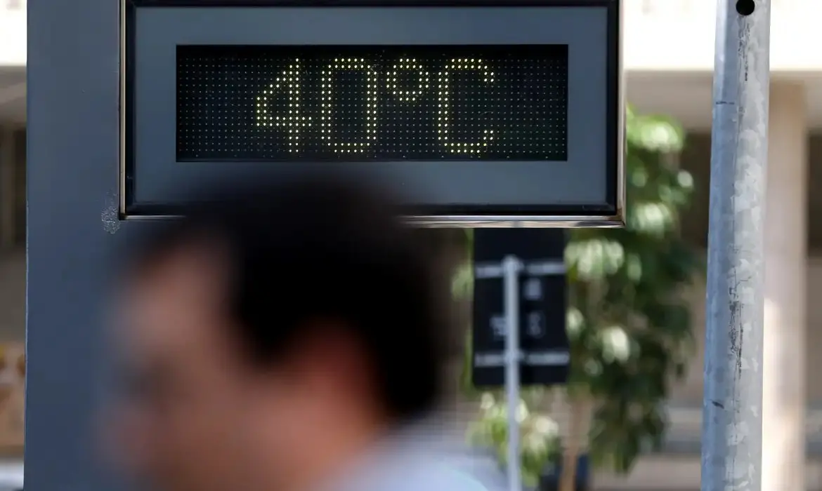 Imagem mostra painel eletrônico de rua exibe a temperatura de 40 °C em um dia de forte calor, com a silhueta desfocada de um pedestre passando em primeiro plano.