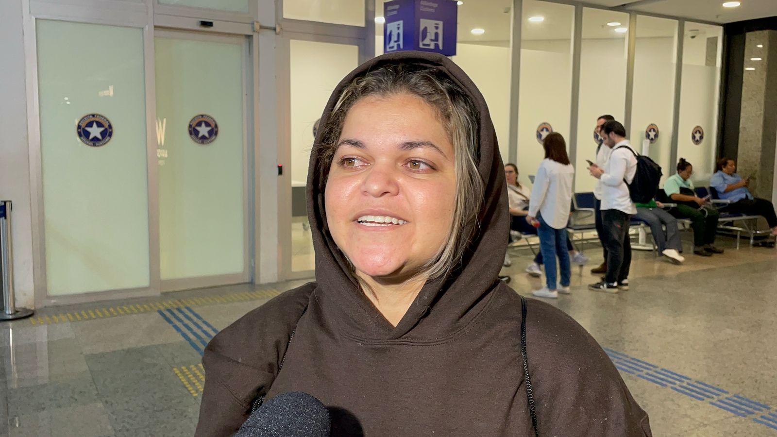 Caroline concede entrevista no aeroporto de Fortaleza. É uma mulher branca de cabelo loiro e está com moletom marrom
