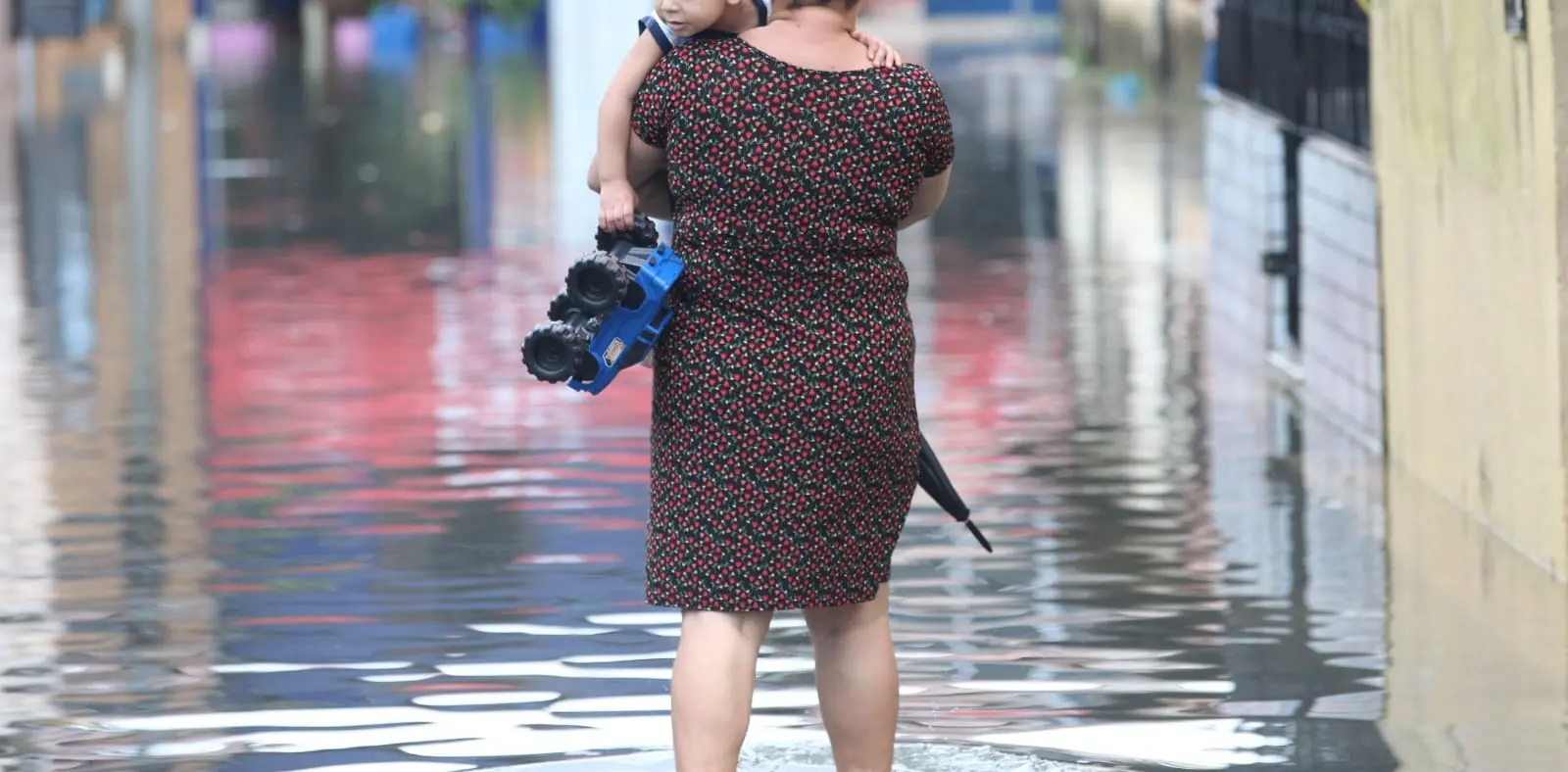 Mulher caminha com criança no braço em rua alagada em Fortaleza