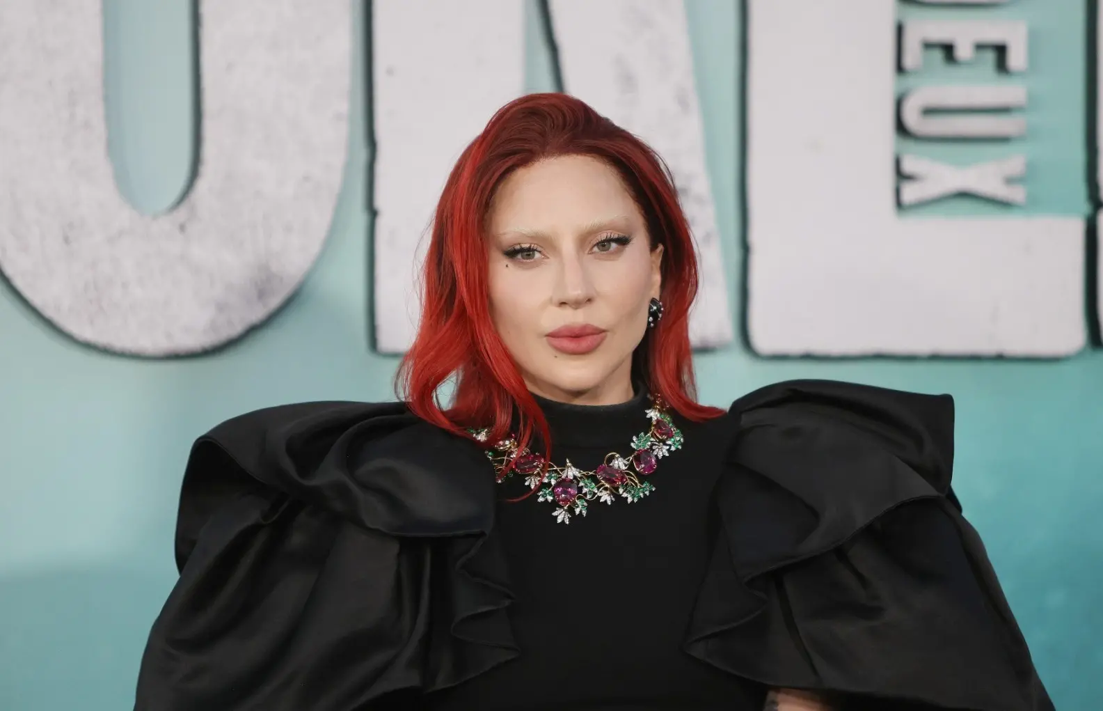 Lady Gaga é uma mulher branca e na foto está de cabelo vermelho e vestido preto com manga bufante