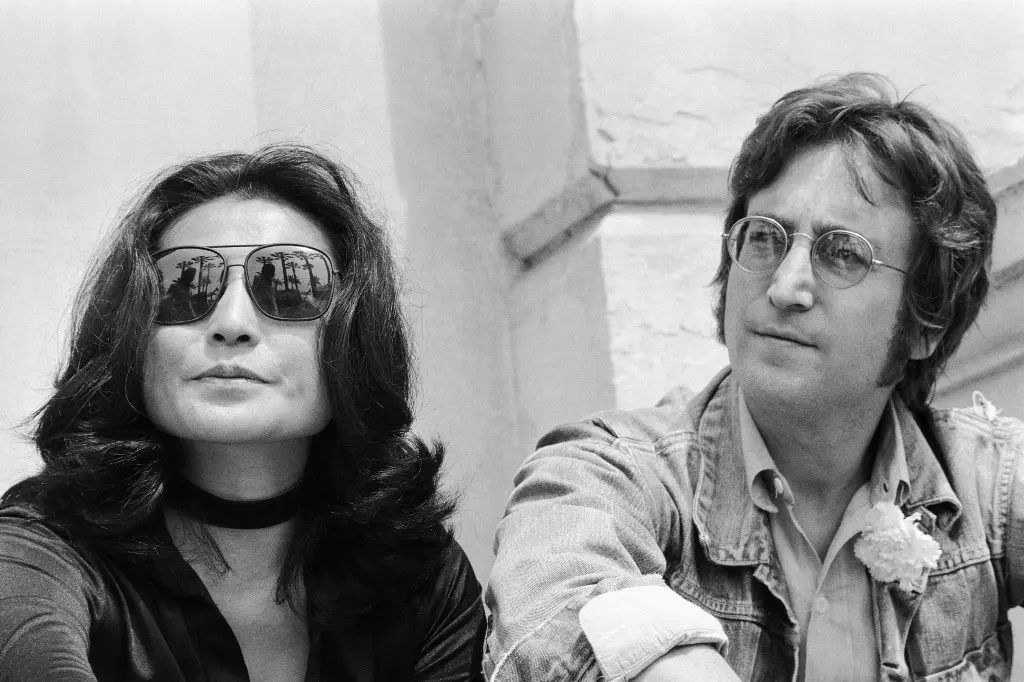 Imagem em preto e branco de John Lennon e Yoko Ono. Eles estão sentados, com Lennon usando óculos e uma camisa jeans, enquanto Yoko usa óculos escuros.