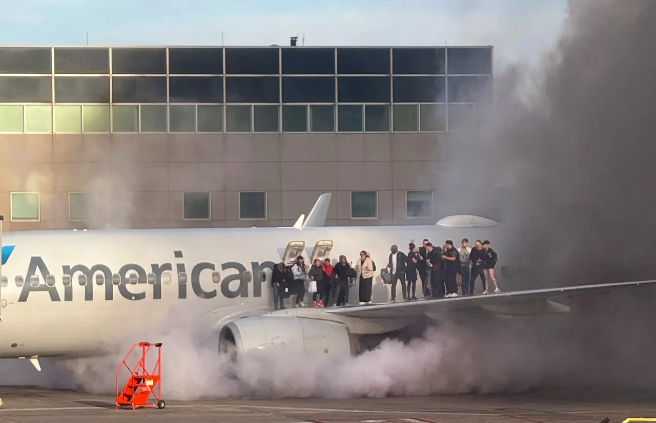 Avião da American Airlines com fumaça e passageiros evacuando pela escada de emergência em uma situação de emergência no aeroporto.