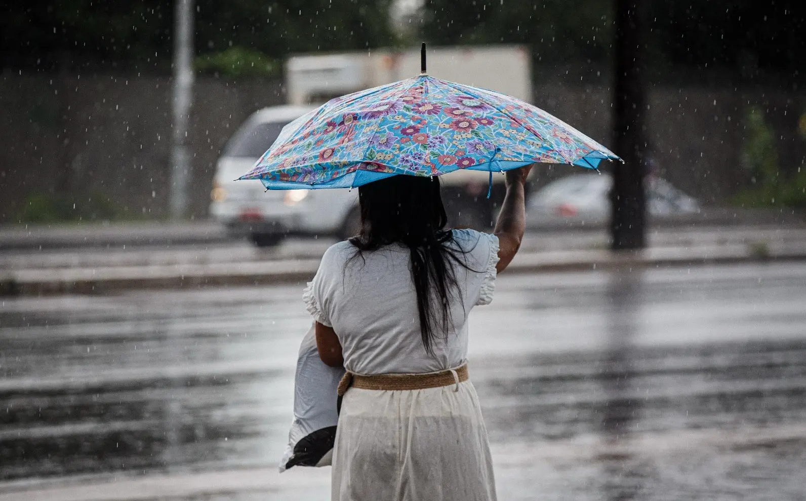 Mulher com guarda-chuva em via pública de costas