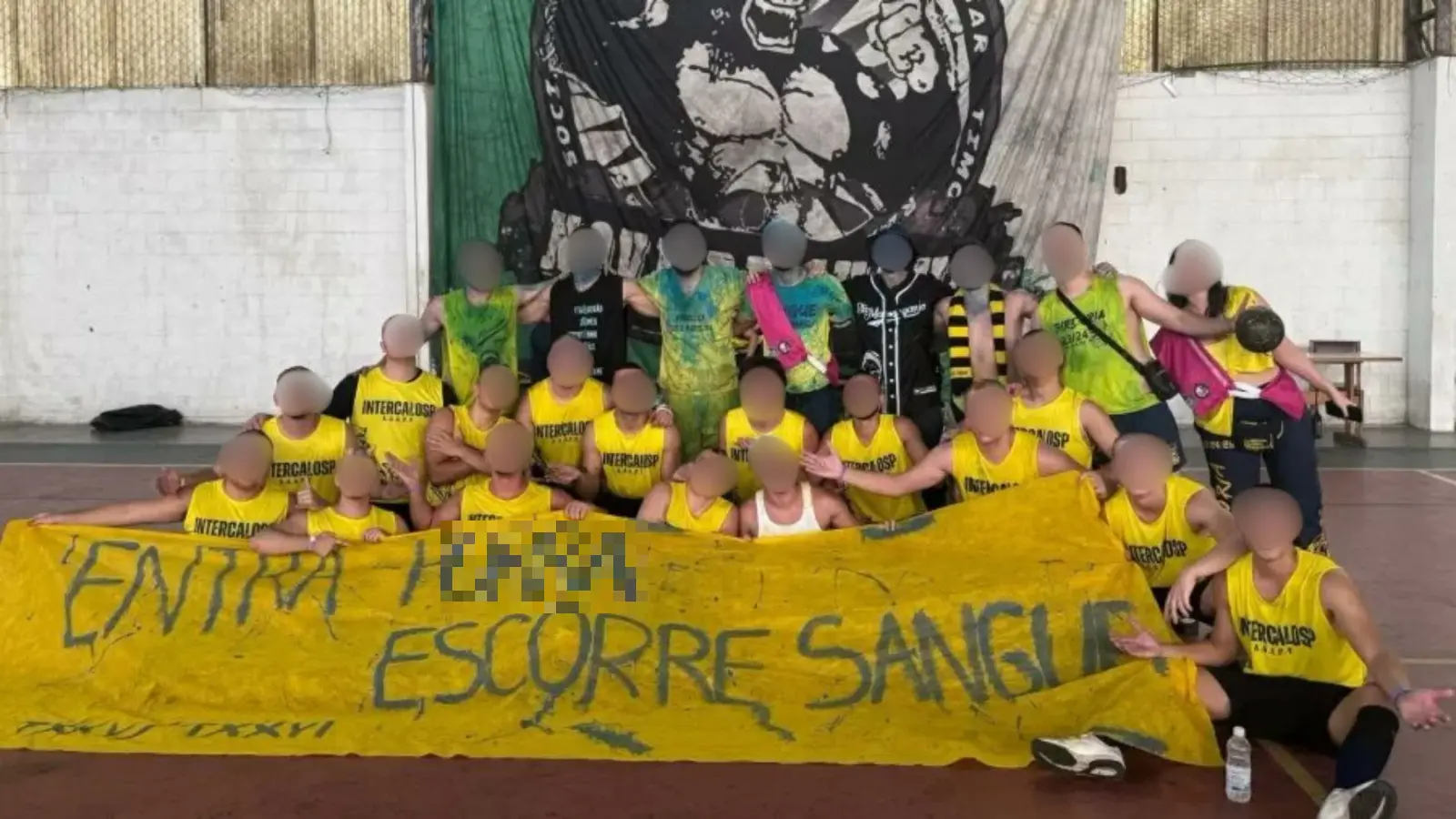 Grupo de torcedores vibrando em um evento esportivo, vestidos com camisas amarelas e segurando uma faixa que contém conteúdos de alusão ao crime de estupro