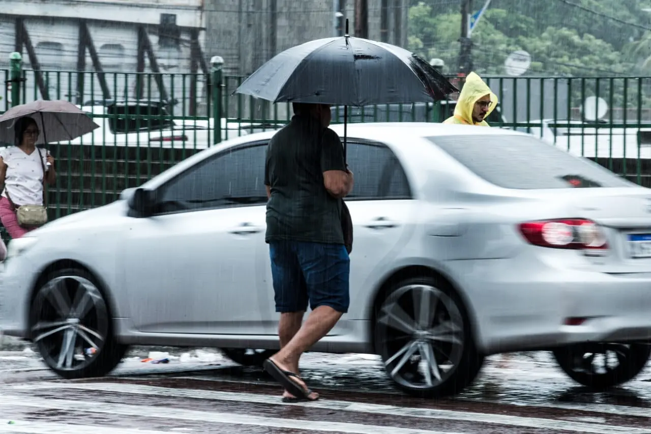Homem atravessa rua com guarda chuva