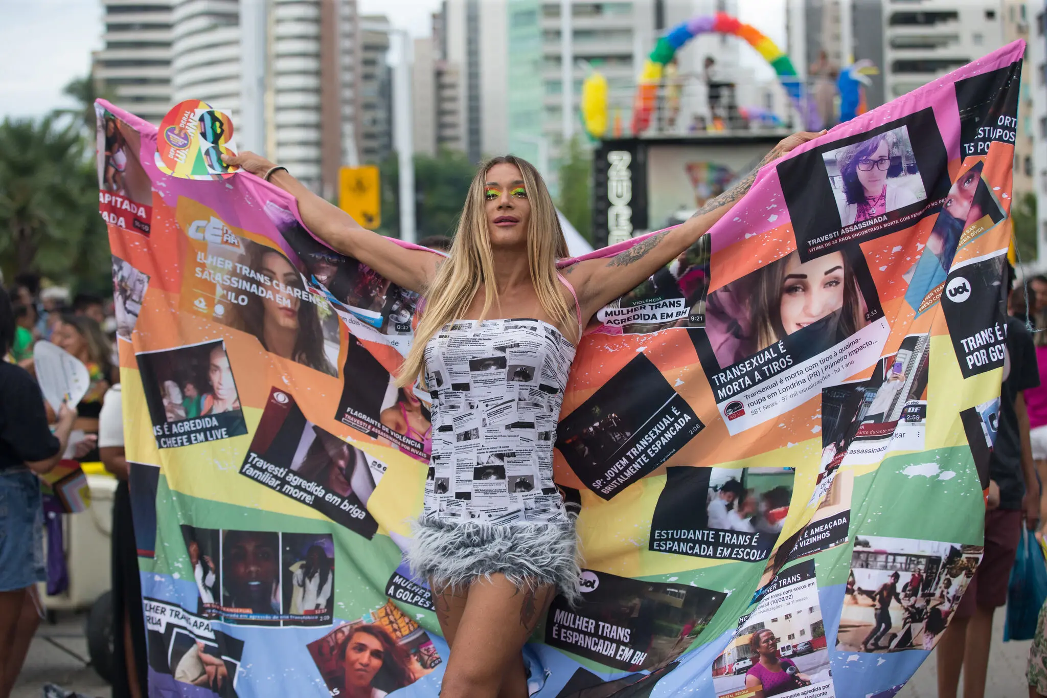 Ativista na parada LGBT 2025 de Fortaleza, com bandeira do arco-iris em que estão coladas chamadas de matérias sobre crimes contra a população LGBTI+