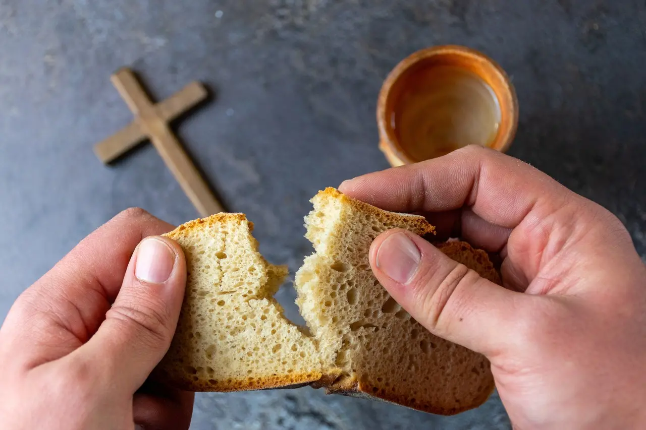 Imagem que mostra uma pessoa quebrando um pão próximo a uma cruz e uma caneca, simbolizando momentos de reflexão e espiritualidade.