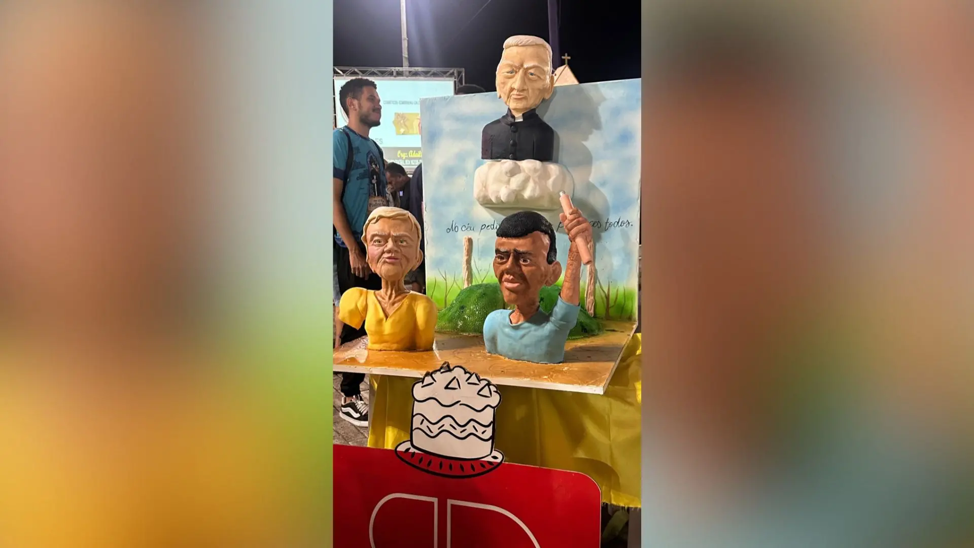 Estatuetas de caricaturas em um evento com três figuras em destaque, incluindo um homem de cabelo grisalho e uma mulher com blusa amarela, em ambiente festivo.