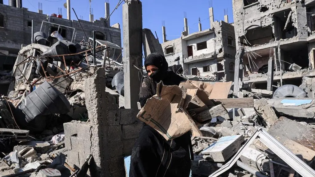 Mulher toda vestida de preto anda entre os escombros de um prédio completamente destruído para matéria sobre proposta de cessar-fogo do Egito em Gaza