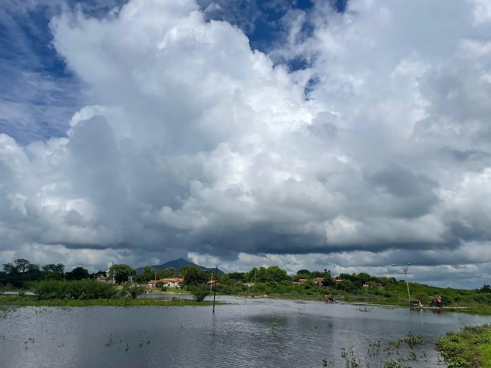 Céu nublado com muitas nuvens sobre o açude Patos, em Sobral, com áreas verdes e residências ao fundo