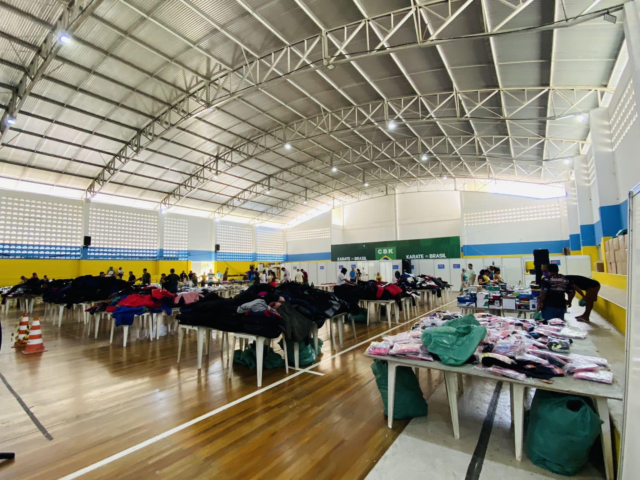 Itens doados pela Receita Federão dispostos em mesas espalhadas pelo que parece ser uma quadra escolar de esportes