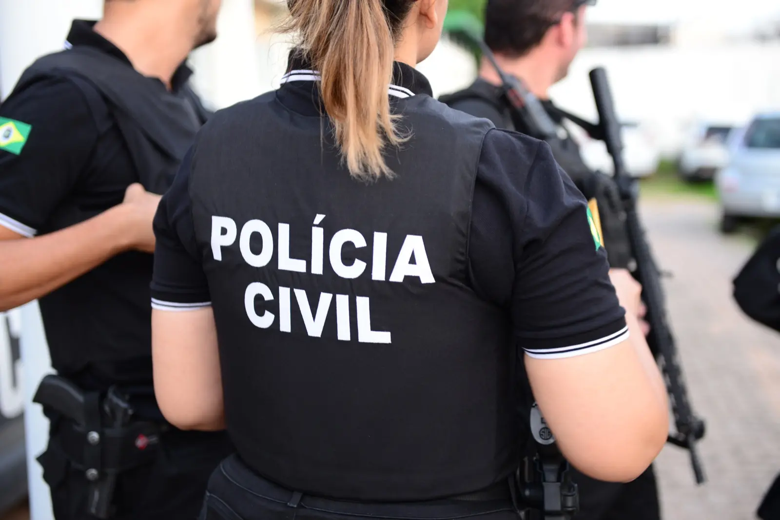 Integrantes da Polícia Civil em ação, com uniforme que destaca a identificação da corporação em um ambiente urbano.