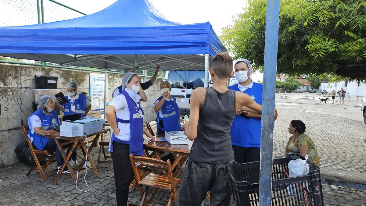 Enfermeiros de máscara e touca atendem homem de camiseta e boné em uma tenda