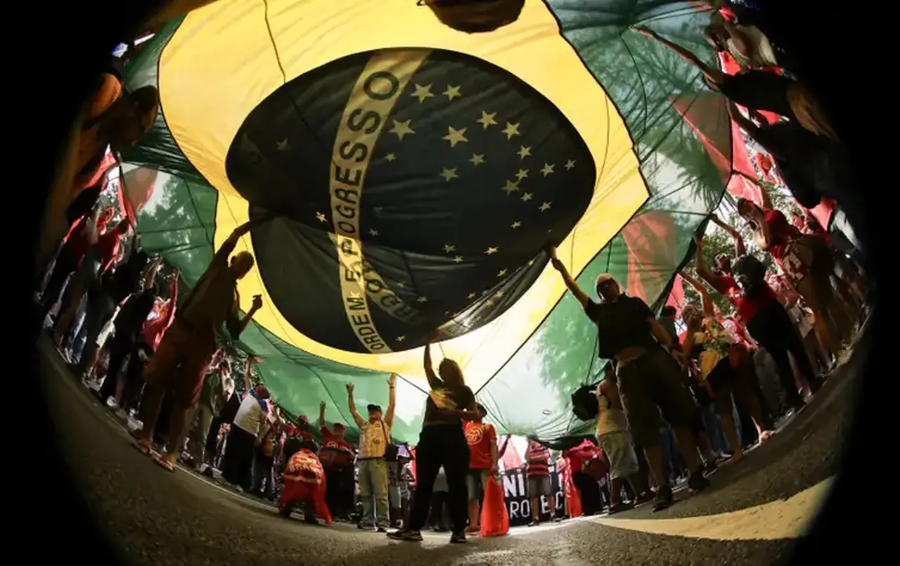 Manifestantes embaixo de uma grane bandeira do Brasil