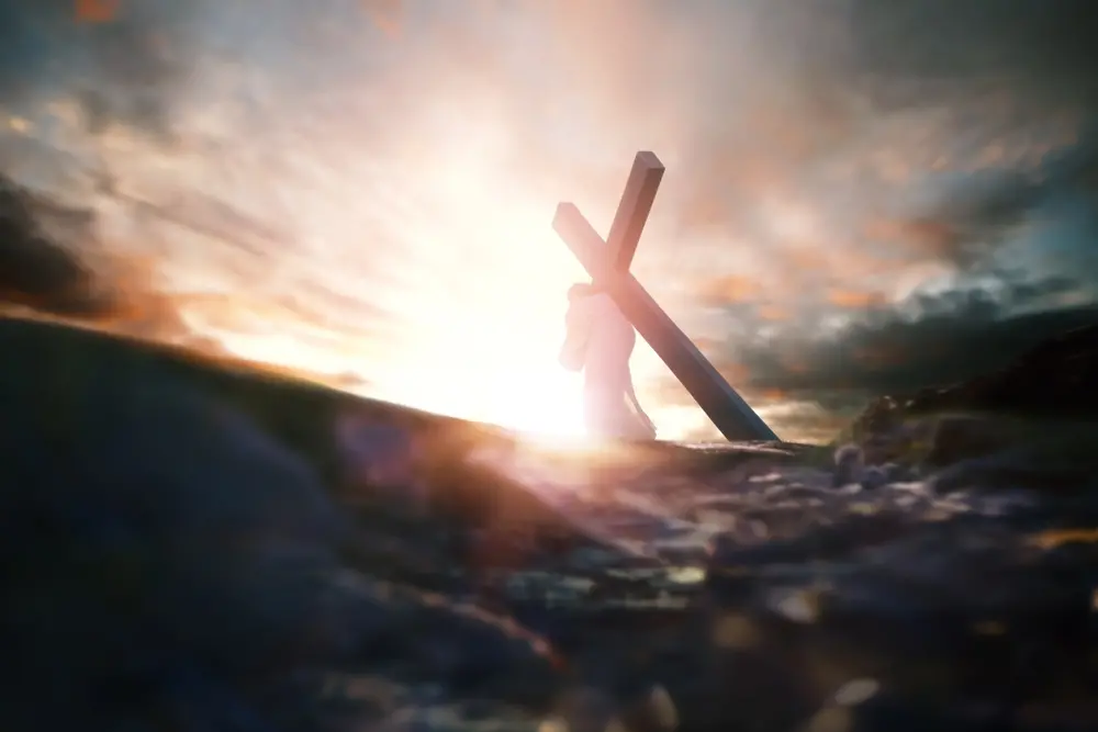 Imagem simbólica de uma figura carregando uma cruz ao amanhecer, representando sacrifício e redenção. Ideal para temas de fé e espiritualidade.