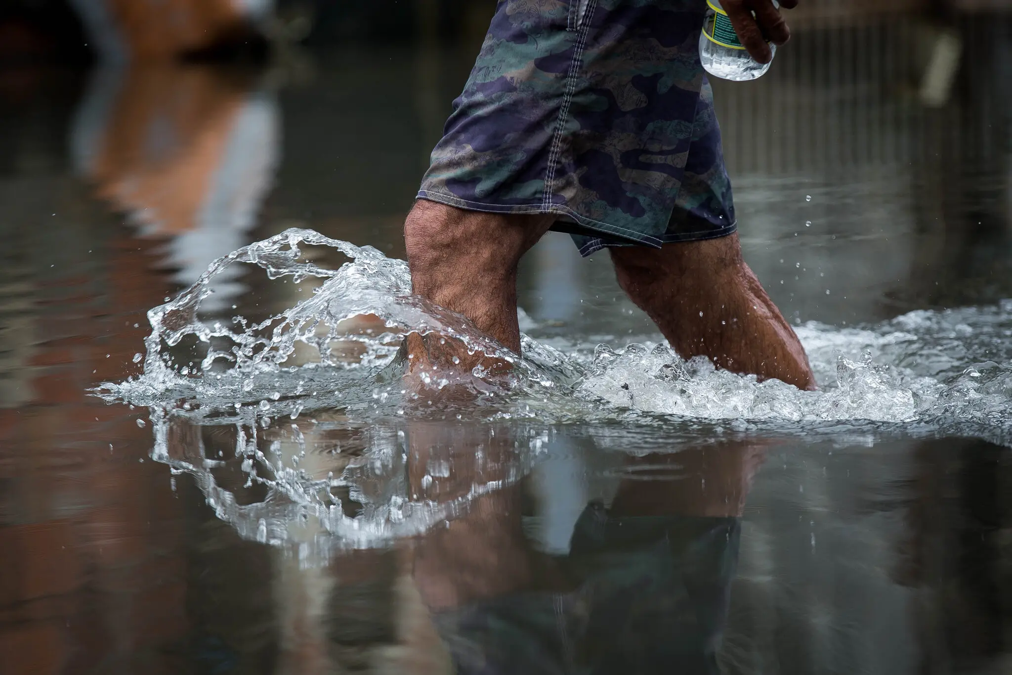 Perna de homem caminhando em rua alagada, com água até próximo do joelho