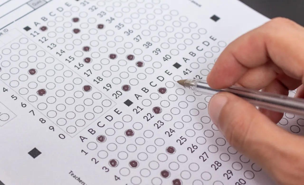 Imagem de uma folha de respostas com questões múltipla escolha. Uma pessoa marca as alternativas com uma caneta, evidenciando a aplicação de um teste.