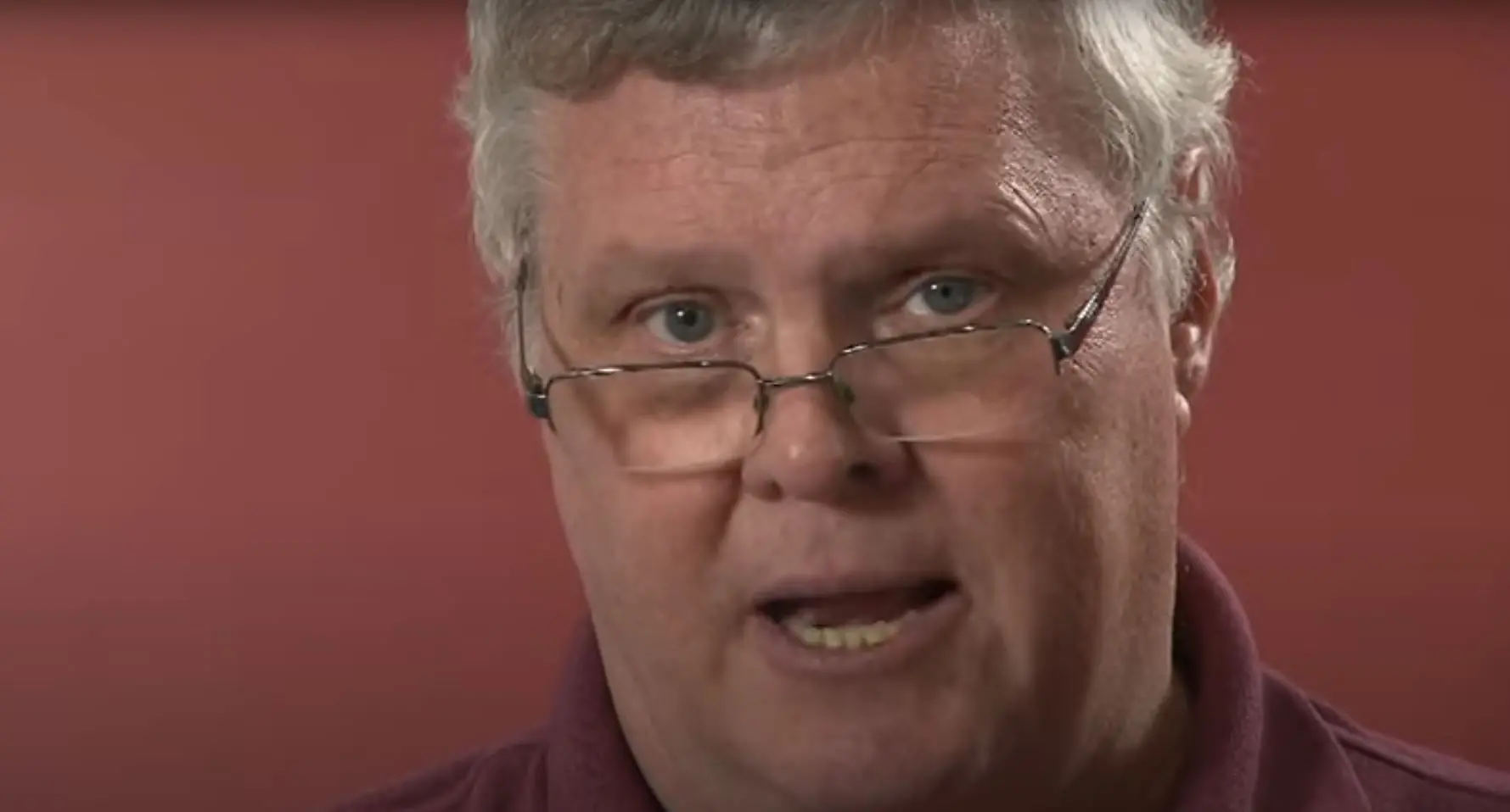 jay north diante de fundo vermelho. ele está em close, e usa óculos