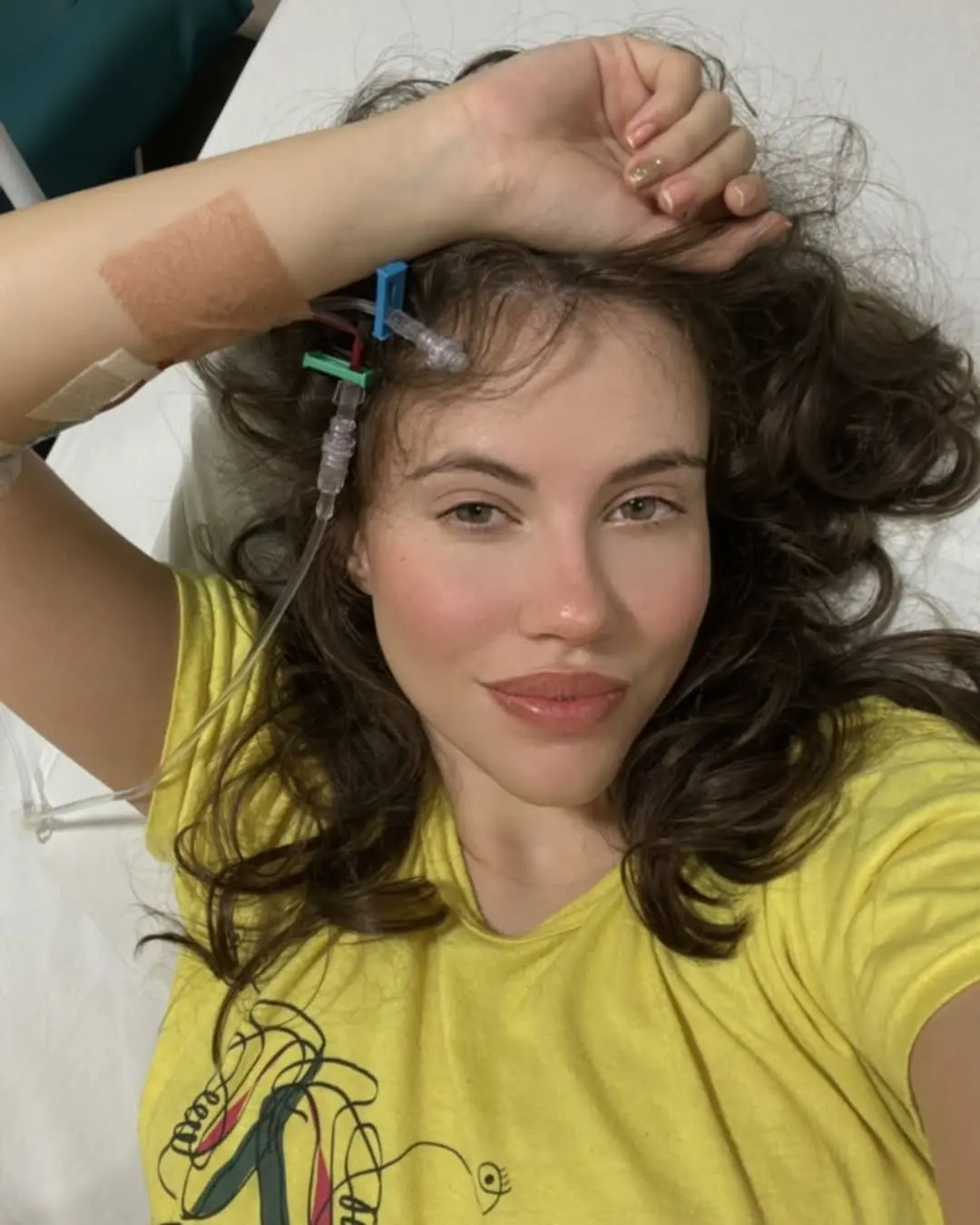 selfie de Sarah Femina mostrando cânulos hospitalares no punho. ela está deitada