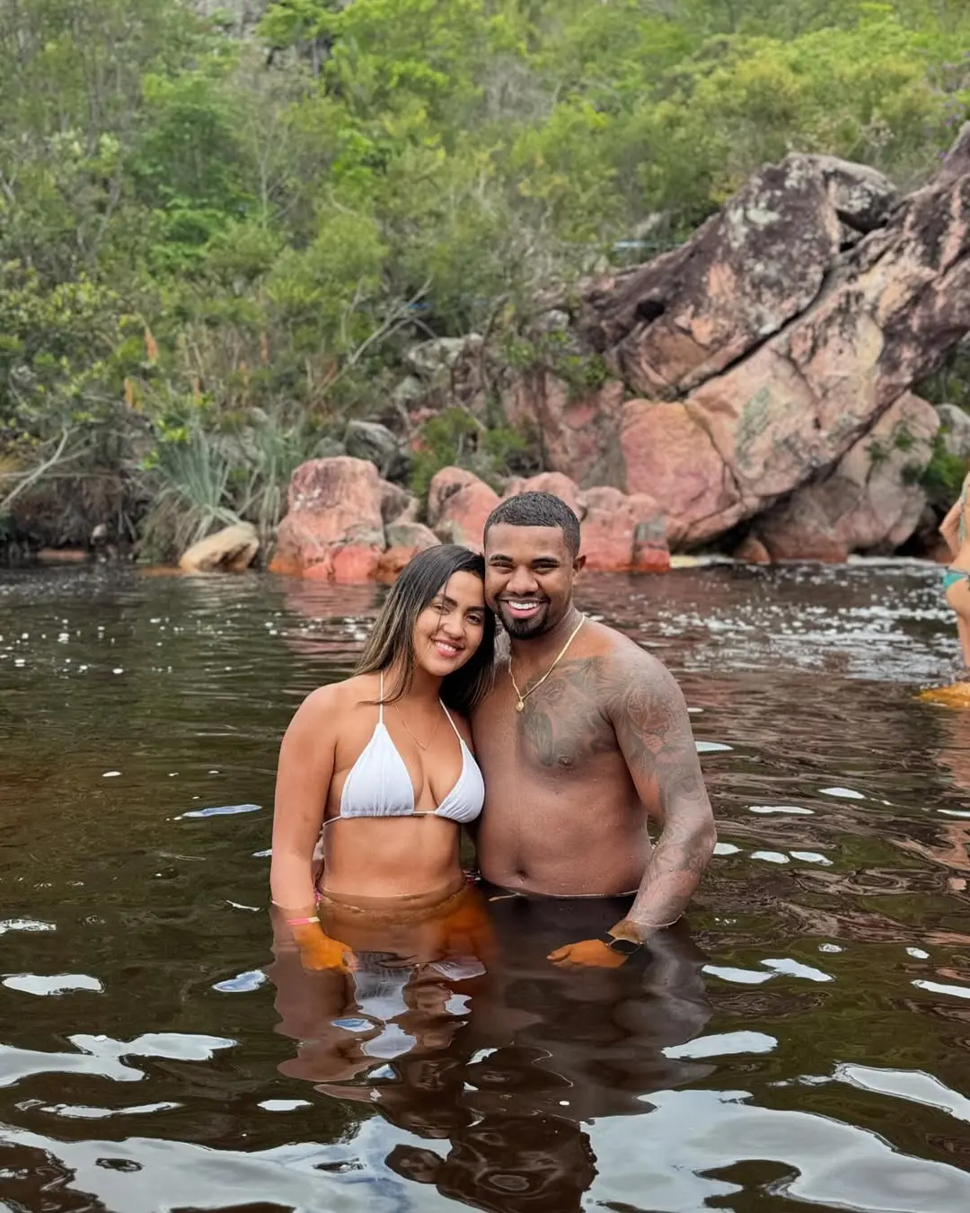 Imagem do ex BBB Davi Brito com a namorada, Adriana Paula, que pediu um tempo no relacionamento dos dois após descobrir gravidez. Eles estão em um ambiente de natureza, com metade do corpo em um lago.