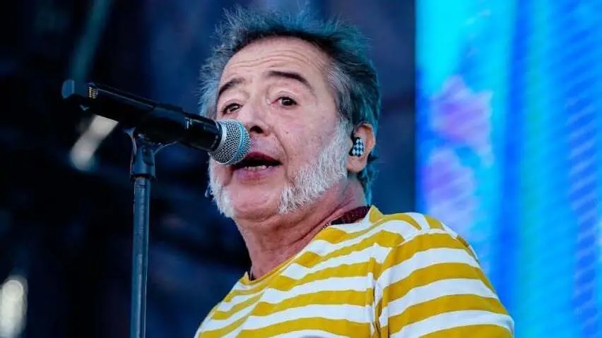 Cantor Nasi da banda Ira! ao microfone usando blusa de listas brancas e amarelas