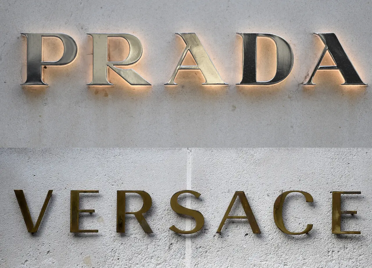 Imagem mostra colagem dos logos das marcas Prada e Versace em fachadas das grifes em alusão ao anúncio de compra da Versace pela Prada