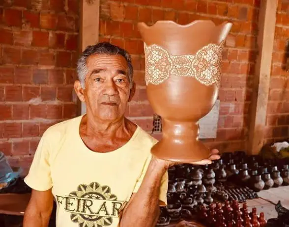 Mestre Muniz era um homem idoso, negro e de cabelo grisalho. Na foto, ele exibe uma escultura de barro