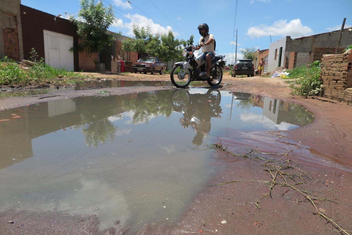 Motoqueiro atravessa uma rua com esgotamento sanitário precária. Na imagem, rua parece alagada