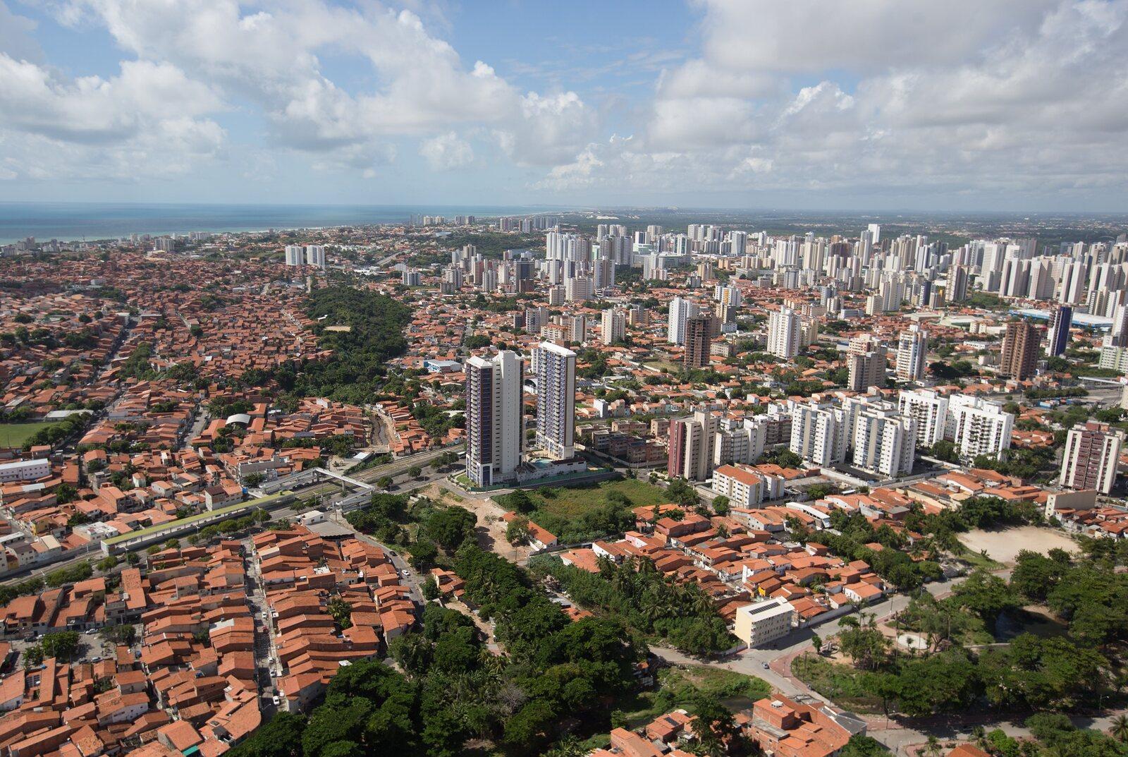 Vista aérea de Fortaleza mostrando bairros residenciais, prédios e condomínios, áreas verdes e o mar ao fundo