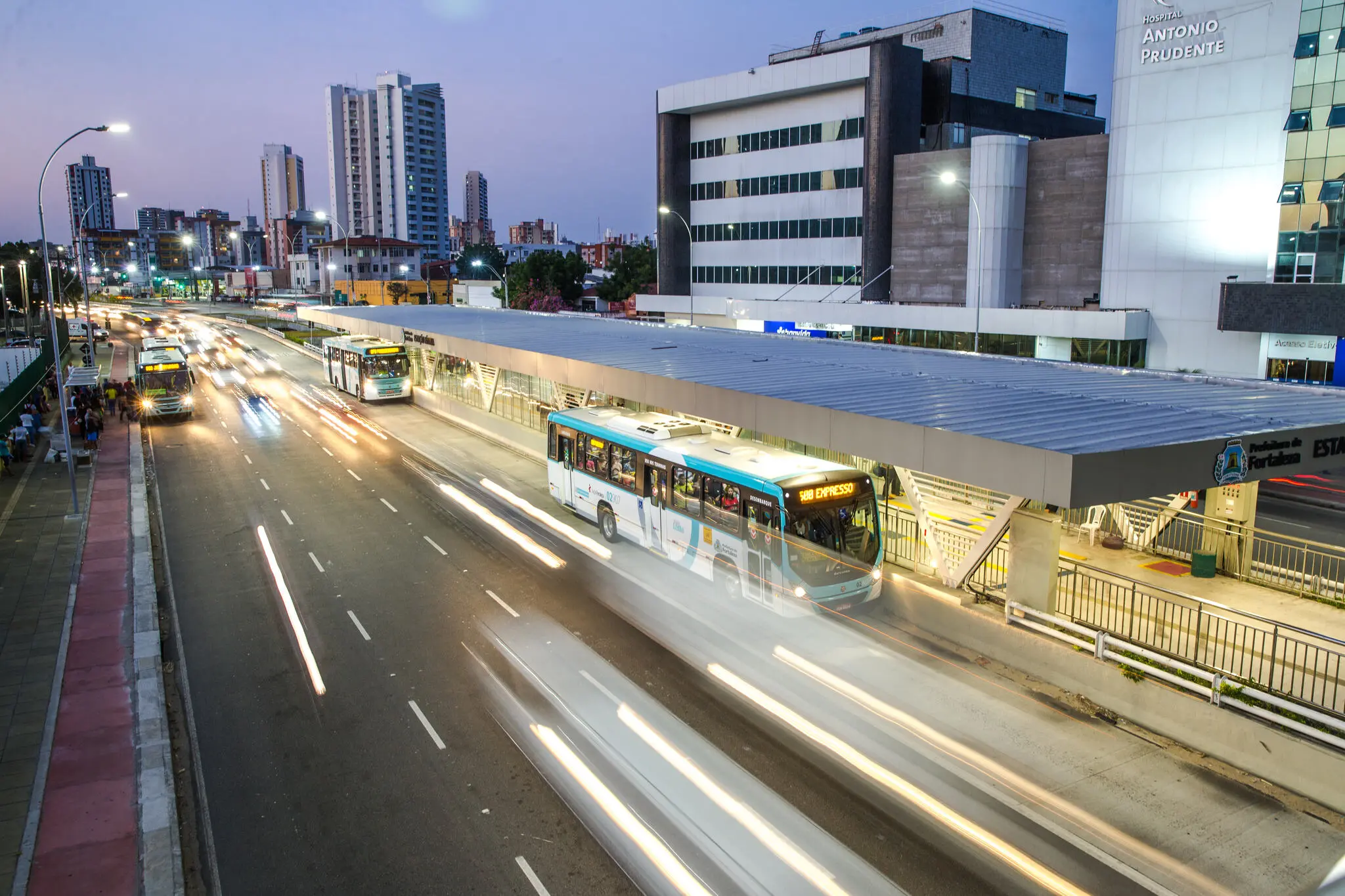 Trânsito na avenida Aguanambi, com carros borrados e rastros de luz, indicando a velocidade dos veículos