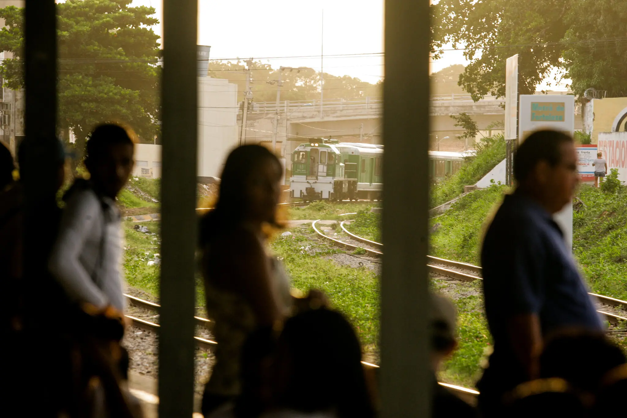 Silhueta desfocada de pessoas esperando o metrô, que aparece ao fundo, em foco