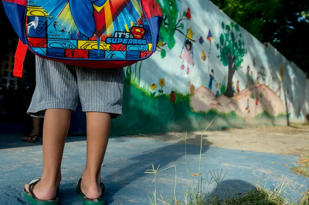 Imagem de criança com um mochila na frente de uma escola pública