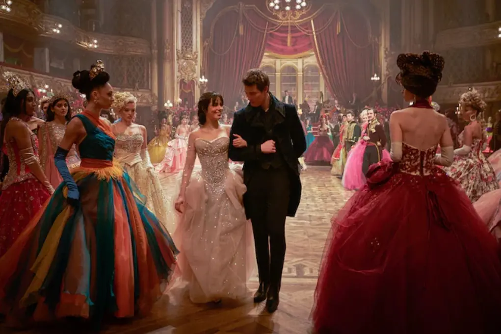 Cenário de baile com pessoas vestindo trajes elegantes e coloridos, destacando um casal dançando no centro da sala. Uma atmosfera de conto de fadas.