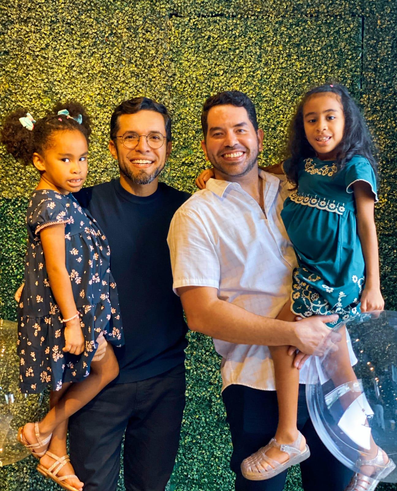 Casal de homens segunrando duas filhas no braço