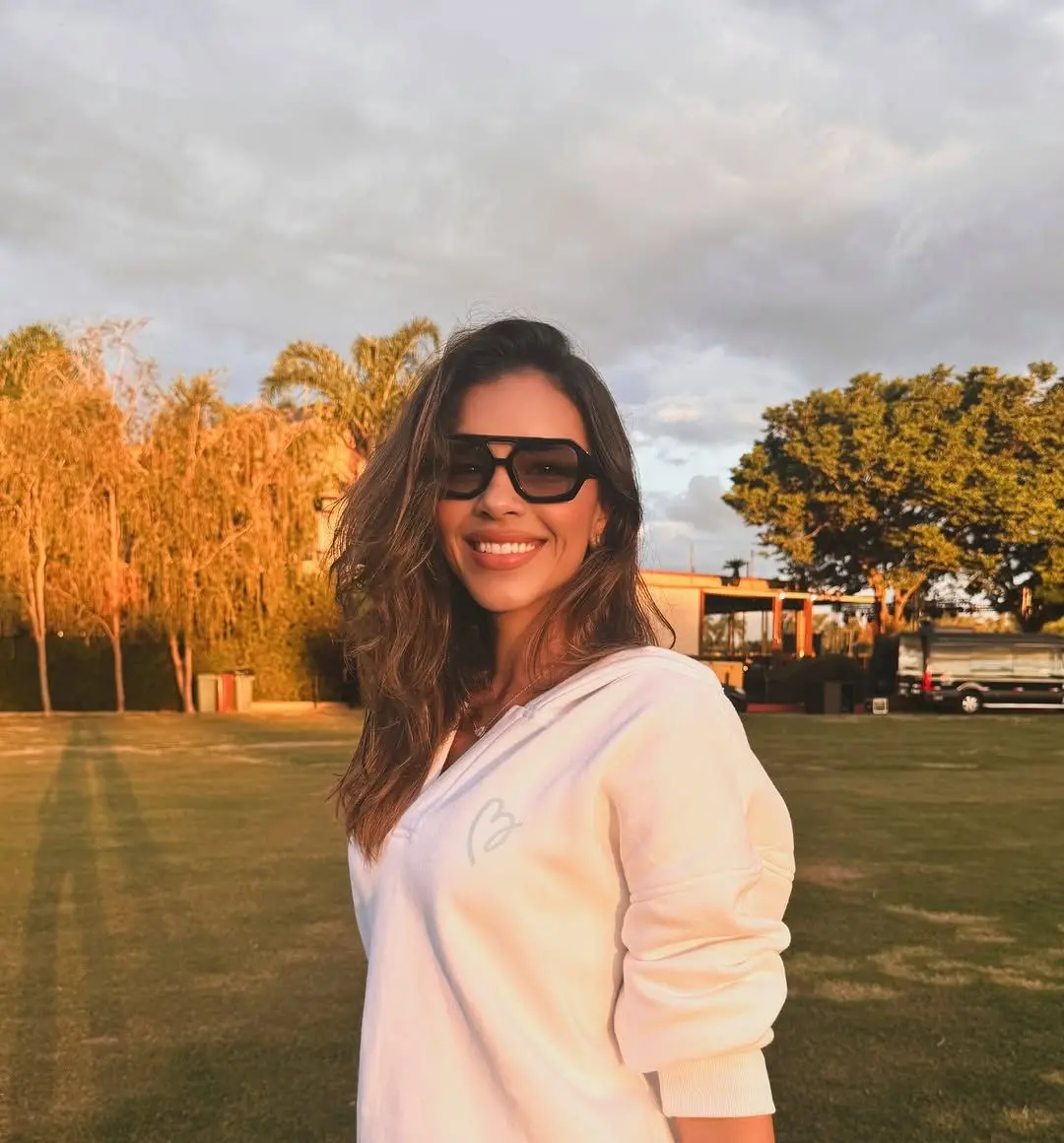 Mariana Rios usando óculos escuros diante de paisagem verde. ela veste roupa branca e sorri