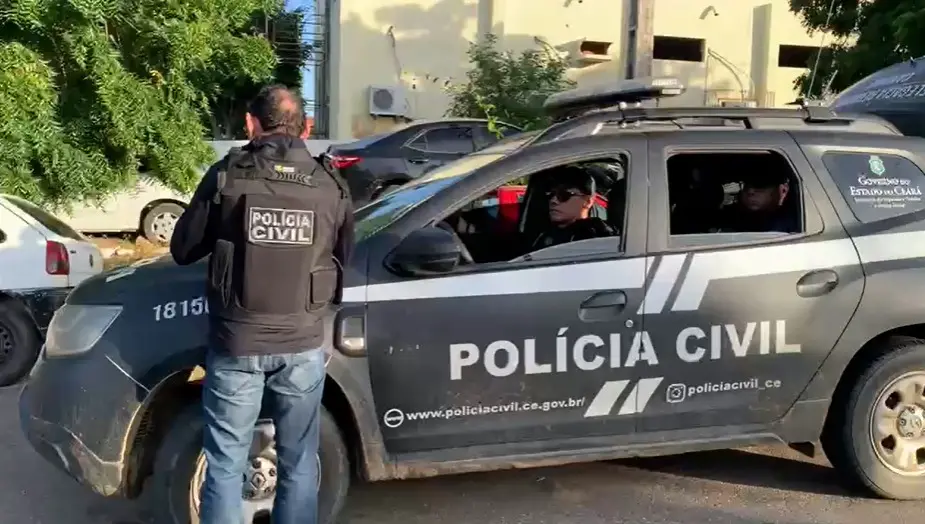 Policiais civis em viatura. Um deles está do lado de fora da viatura e de costas