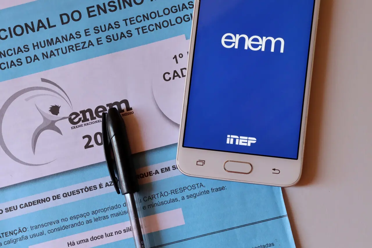 Imagem mostrando a prova do ENEM junto a um celular exibindo o logo do ENEM e uma caneta, ideal para estudantes e educadores sobre o exame