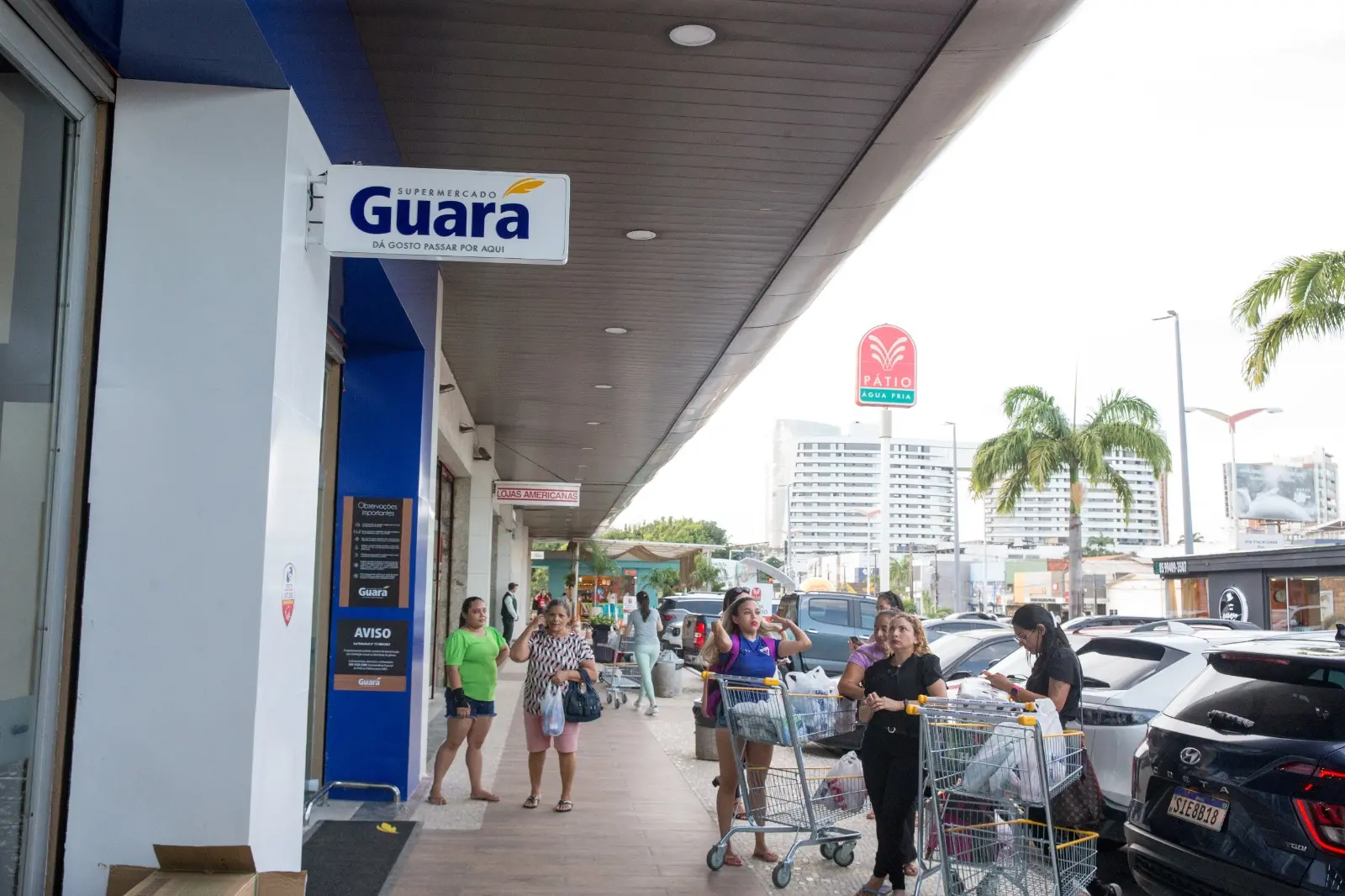 Foto que contém uma loja de uma fachada lateral do Supermercado Guará, com nome em azul com detalhe em amarelo acima da última letra 
